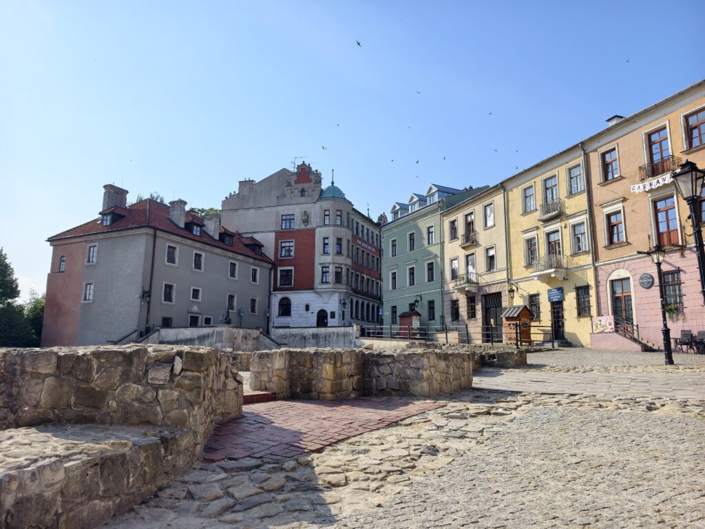Widok na kolorowe kamienice otaczające Plac Po Farze w Lublinie oraz fragment odsłoniętych fundamentów dawnego kościoła