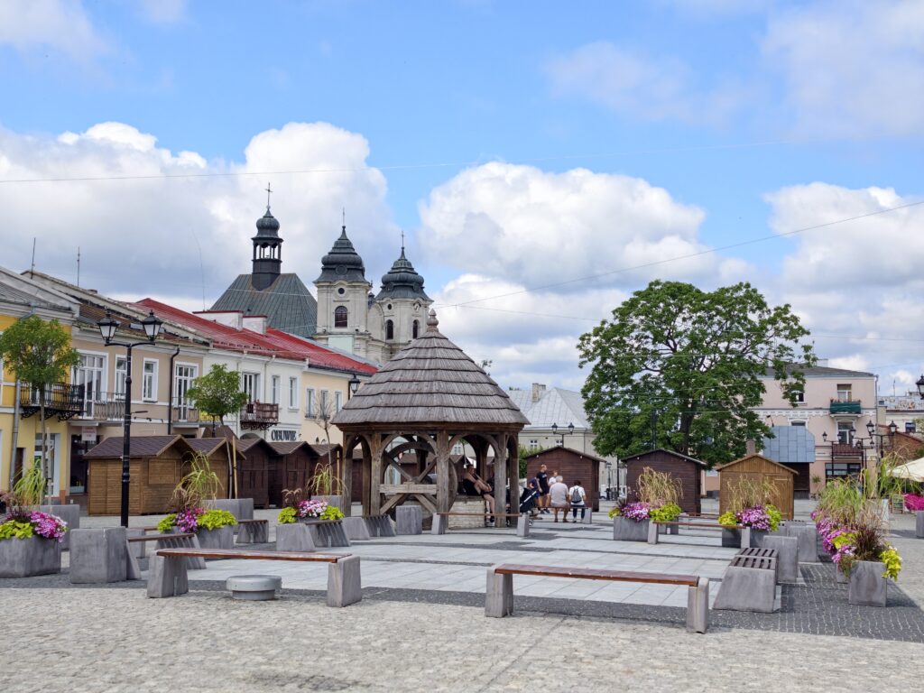 Plac Łuczkowskiego w Chełmie z drewnianą, zrekonstruowaną studnią i widocznymi w tle wieżami kościoła