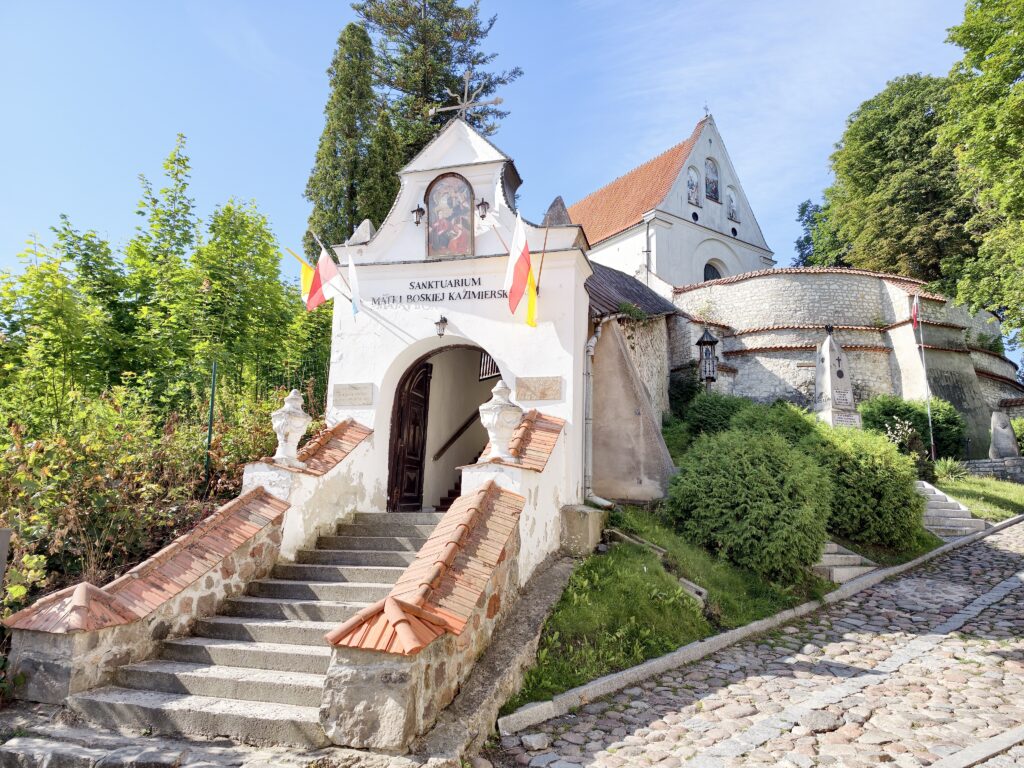 Wejście do Sanktuarium Matki Boskiej Kazimierskiej z kamiennymi schodami i flagami Polski