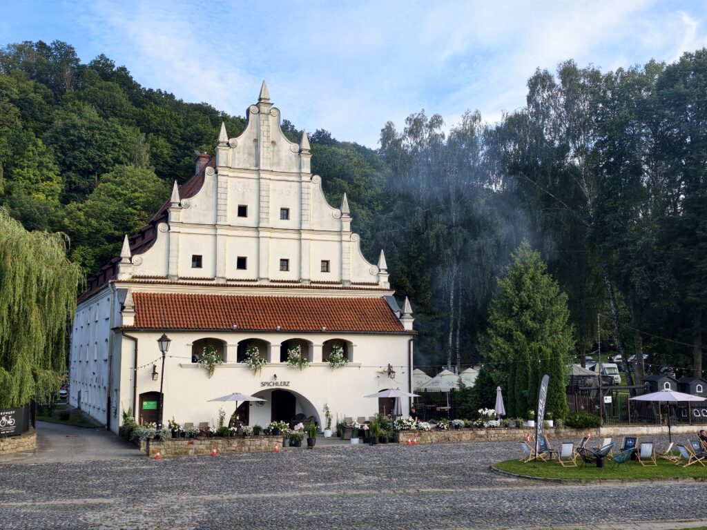 Zabytkowy biały spichlerz z czerwonym dachem i ogródkiem restauracyjnym w Kazimierzu Dolnym