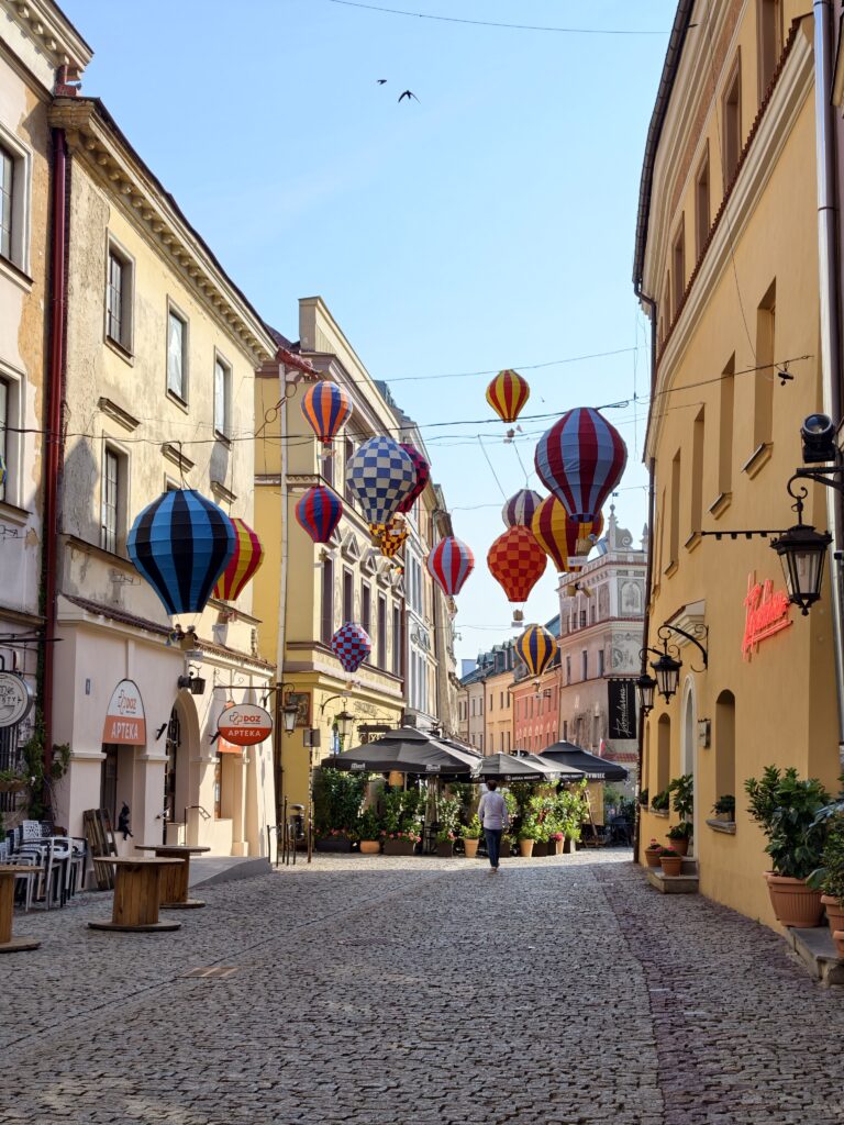 Wąska, brukowana uliczka lubelskiego Starego Miasta z zawieszonymi nad nią kolorowymi balonami dekoracyjnymi