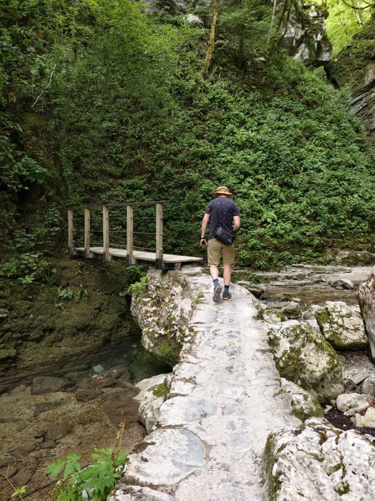 Turysta idący drewnianą kładką nad potokiem na szlaku do wodospadu Kozjak