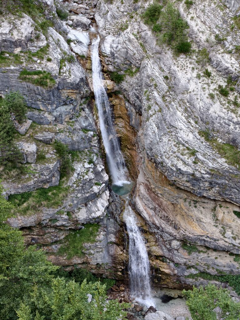Wodospad Mangartski spadający kaskadami po stromych, warstwowych ścianach skalnych w Alpach Julijskich, ze zbliżeniem na naturalne formacje.