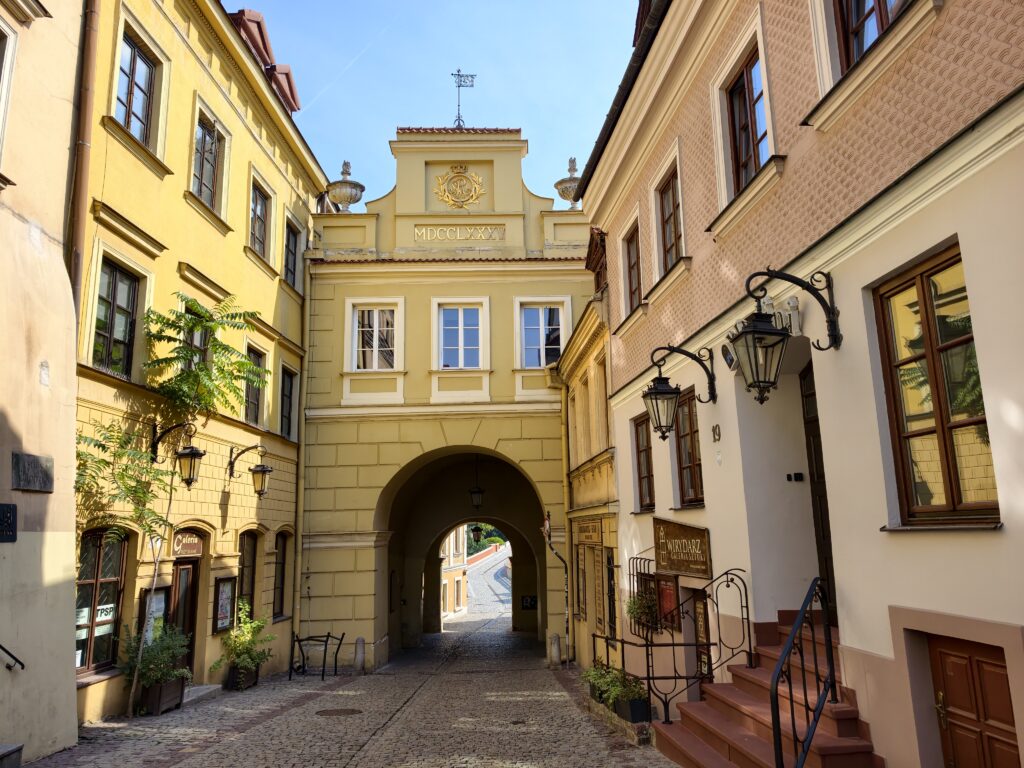 Żółta, zabytkowa brama Grodzka przejazdowa z inskrypcją MDCCLXXXV prowadząca na wąską uliczkę Starego Miasta w Lublinie