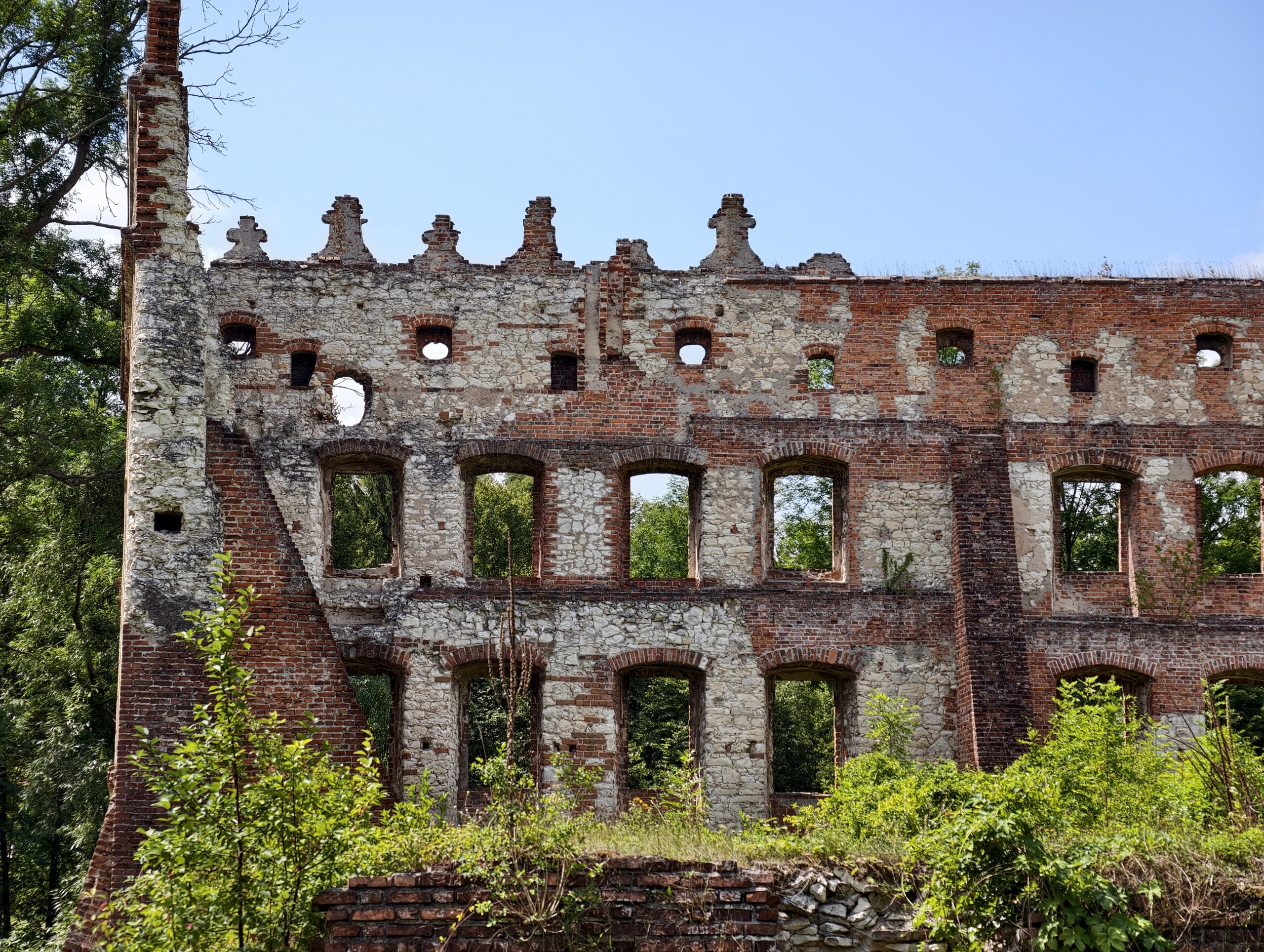 Fragment murów zamku w Krupem z ozdobną attyką i rzędami okien w ceglano-kamiennej ścianie