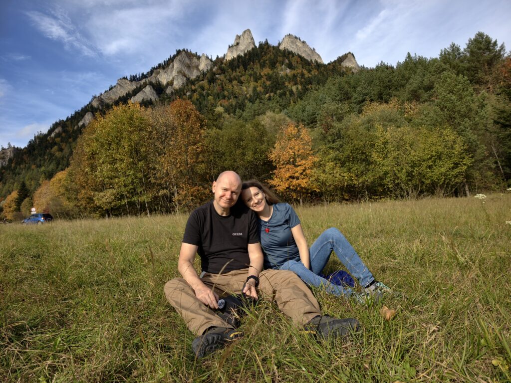 Autorzy bloga Duet na szlaku siedzą na łące u stóp Trzech Koron, za nimi jesienne drzewa i wapienne turnie