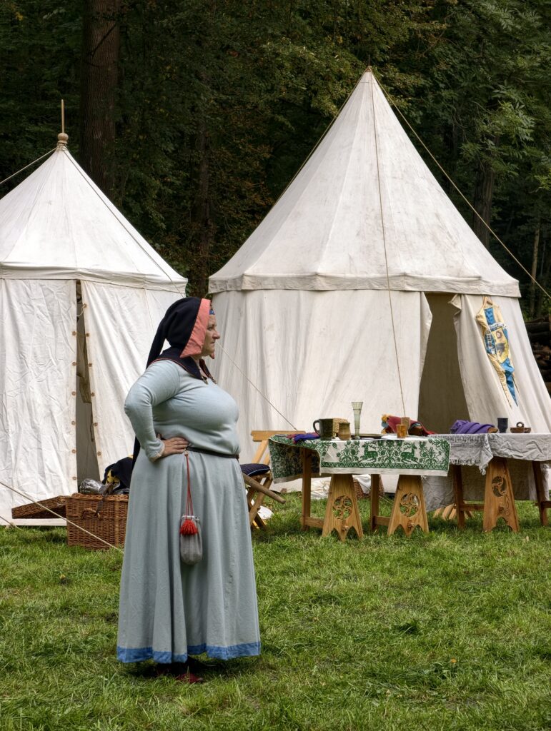 Rekonstruktorka w średniowiecznym stroju przed białymi namiotami w obozowisku Juromanii pod zamkiem Korzkiew