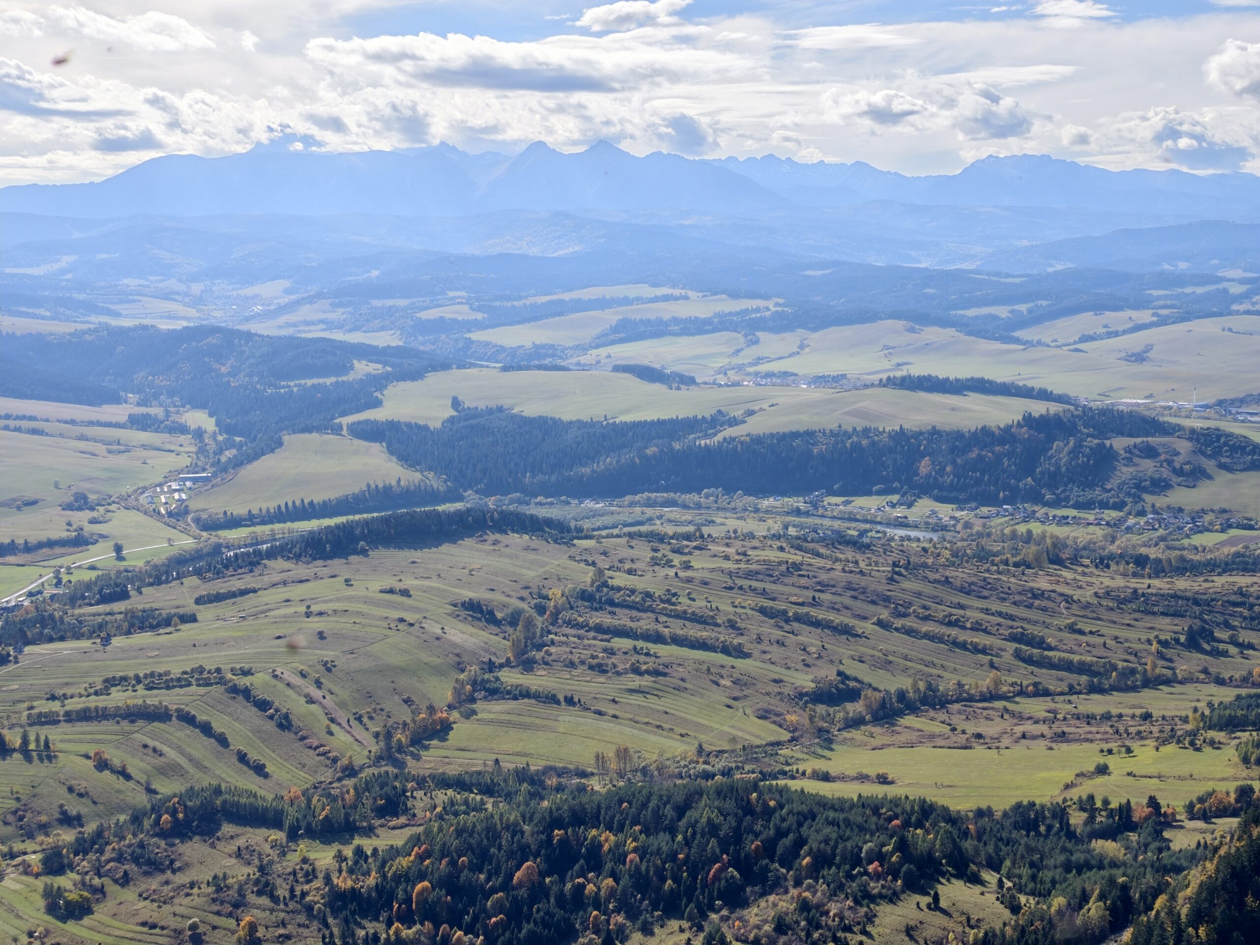 Panorama Tatr widziana z Trzech Koron ponad wsiami i pasiastymi polami po słowackiej stronie Dunajca