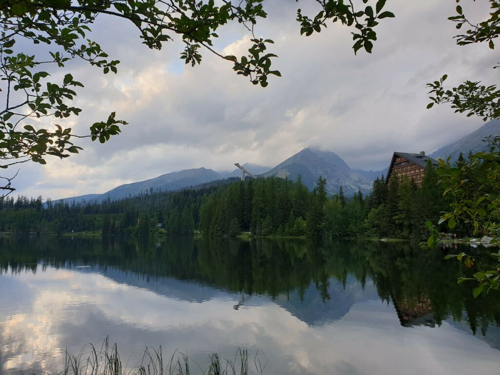 Las, hotel Patria i skocznie narciarskie odbijają się w gładkiej tafli jeziora w pochmurny wieczór