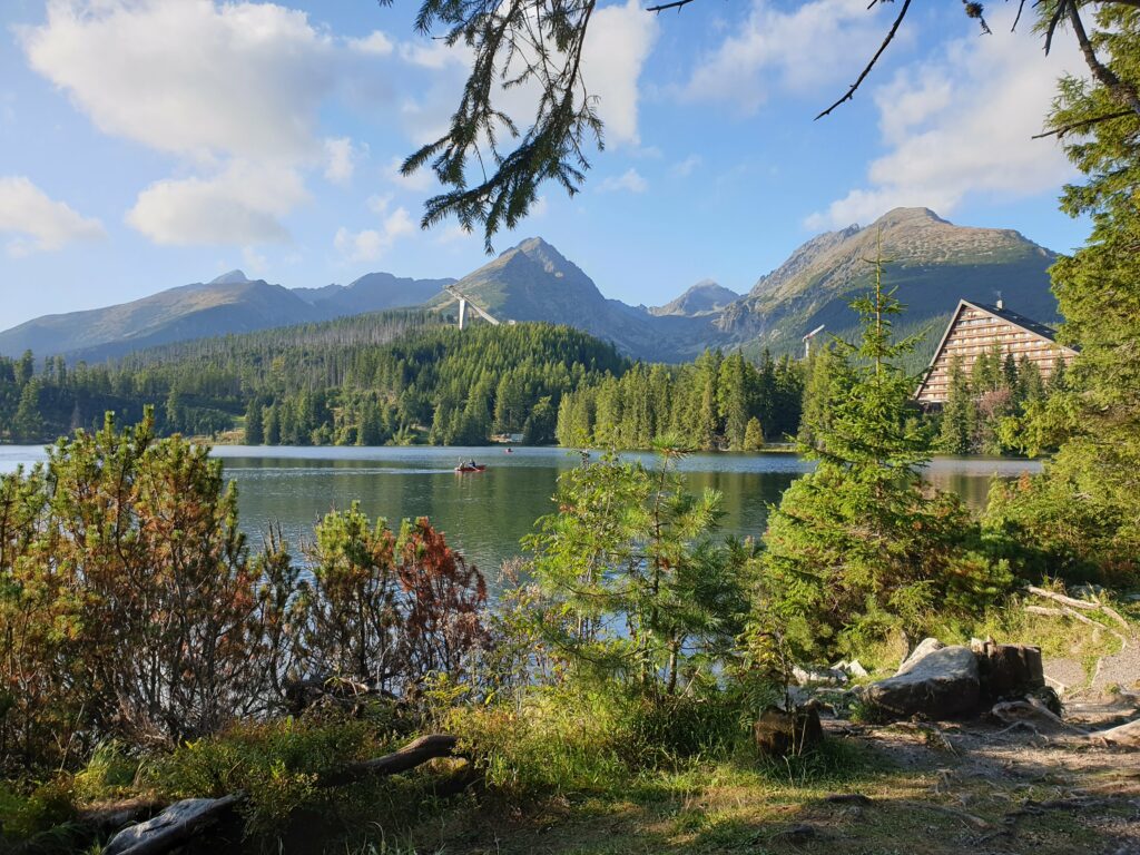Jezioro we wrześniu: kosodrzewina i czerwieniejące krzewy na brzegu, w tle skocznie, hotel Patria i Tatry