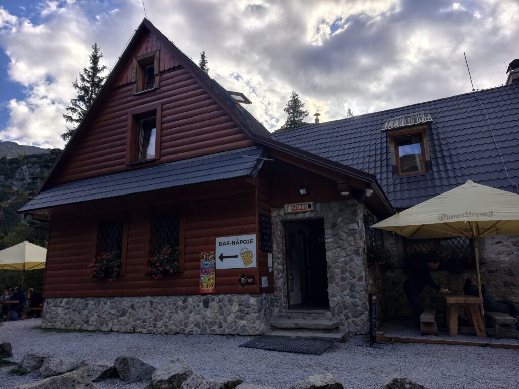 Drewniano-kamienny budynek Ťatliakovej chaty z napisem Bar–Nápoje oraz parasolami i stolikami przed wejściem