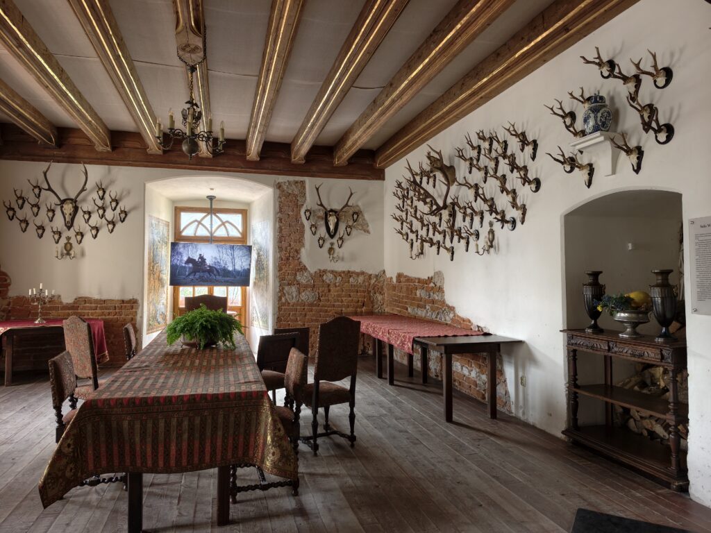 Sala w Zamku Korzkiew z porożami na ścianach, długim stołem, belkowym stropem i odsłoniętą cegłą