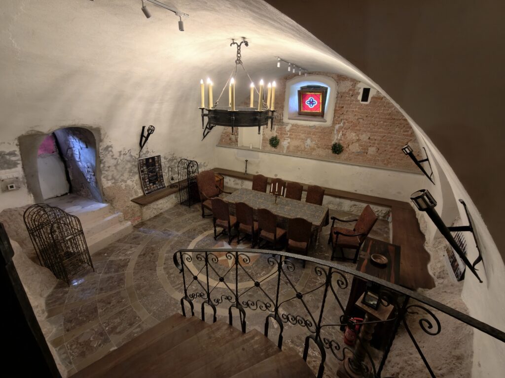 Sklepiona piwnica Zamku Korzkiew ze stołem, żyrandolem ze świecami i kamienną posadzką ze wzorem gwiazdy